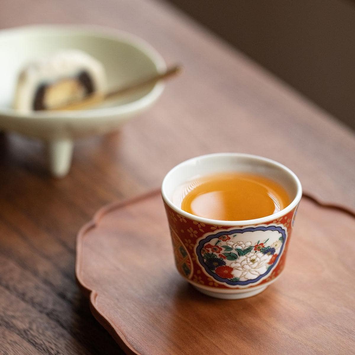 Japanese Kutani ware cups with cartoon and floral motifs on a wooden table.