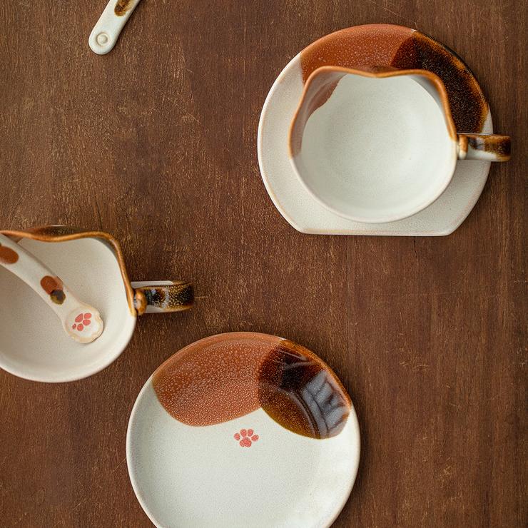 Two ceramic cat-themed coffee cups on a wooden surface