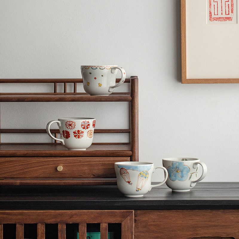 Ceramic mugs with floral and balloon designs on a wooden shelf