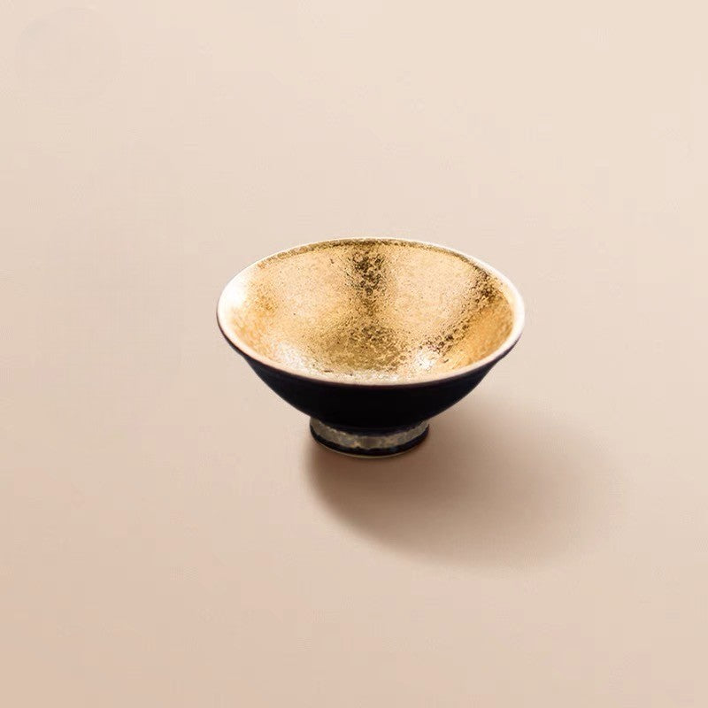 Luxurious ceramic sake cup with golden interior and black exterior.