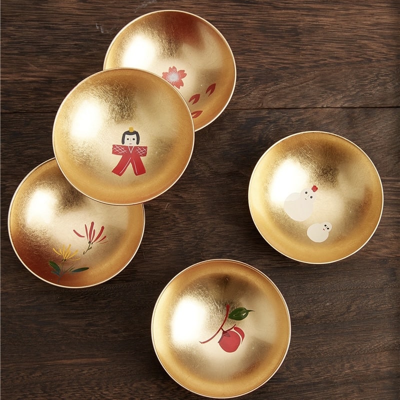 Japanese lacquerware sake cup set with gold-leaf interiors and colorful motifs.