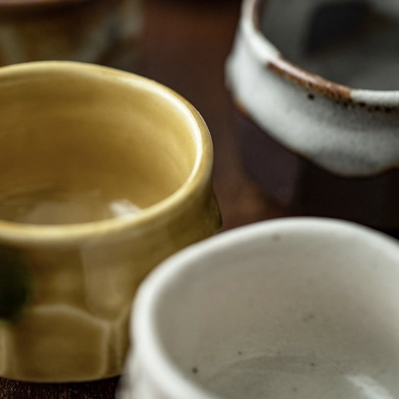 Close-up of six textured ceramic tea cups in earthy tones.