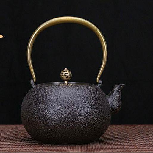 Black cast iron tea pot with textured finish and polished brass handle.