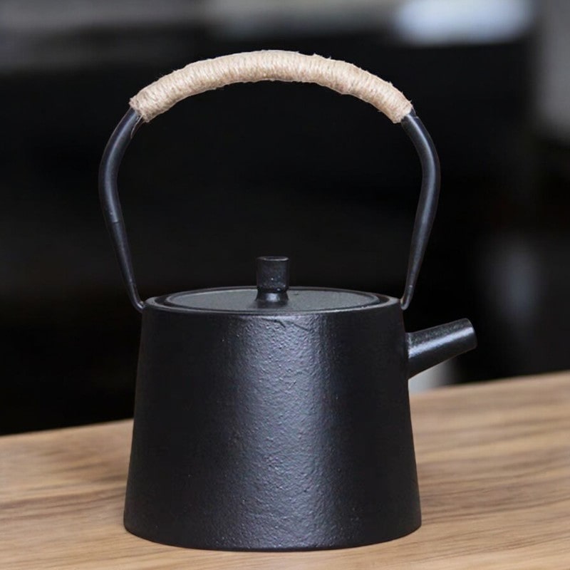 Minimalist black cast iron tea pot with a woven handle on a wooden table.