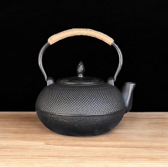 Close-up of a textured black cast iron tea pot with ergonomic handle.