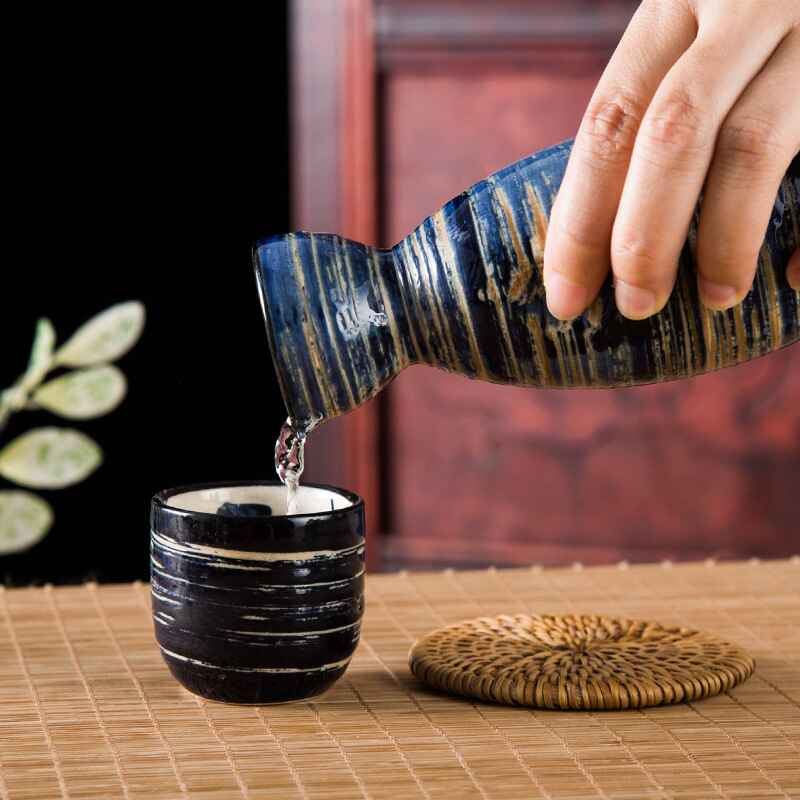 Handcrafted sake drinking set with a bottle and matching cups on a bamboo mat.