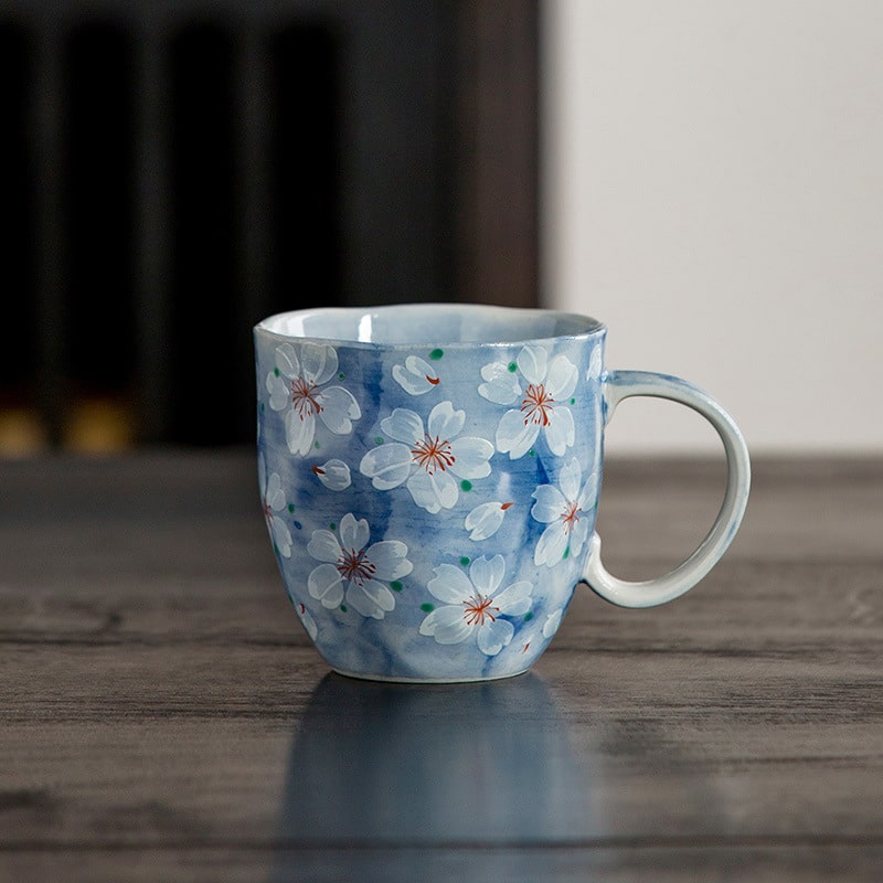 Blue hand-painted cherry blossom coffee cup on a wooden table.