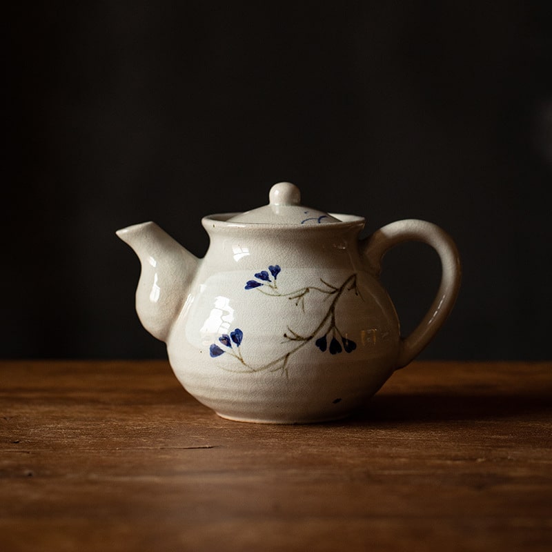 Japanese ice crack ceramic teapot with blue floral pattern on a wooden table.