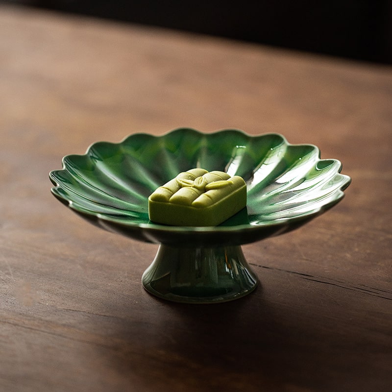 Elevated green ceramic plate with pedestal design for serving desserts.