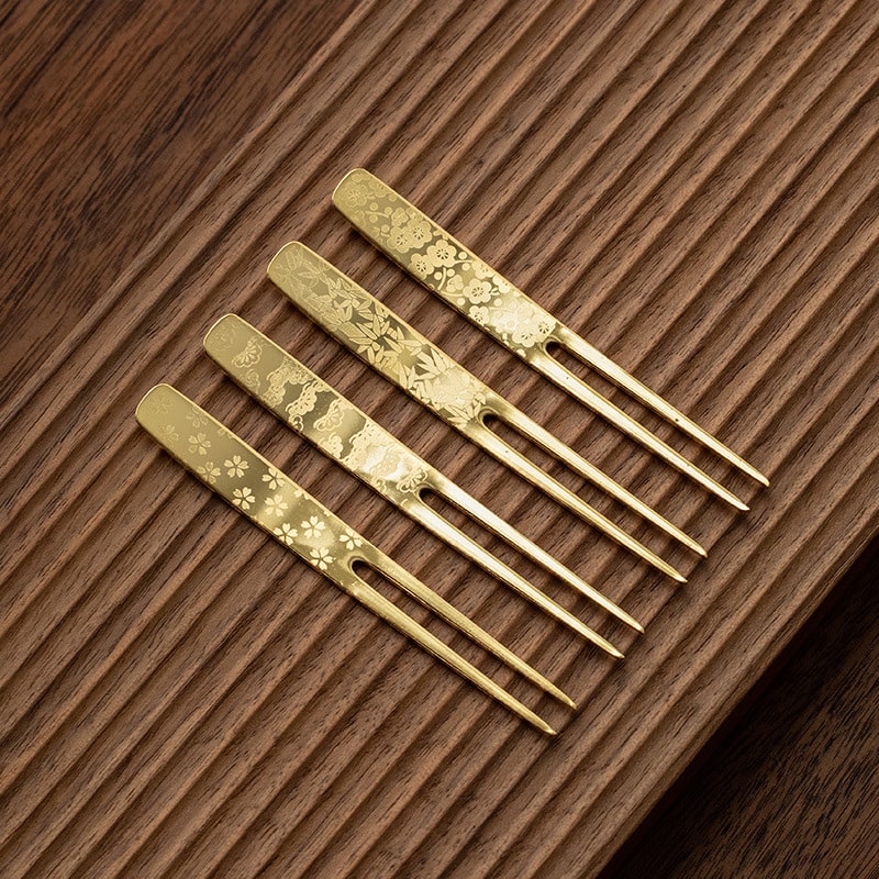 Hand holding a gold-plated dessert fork with floral engravings