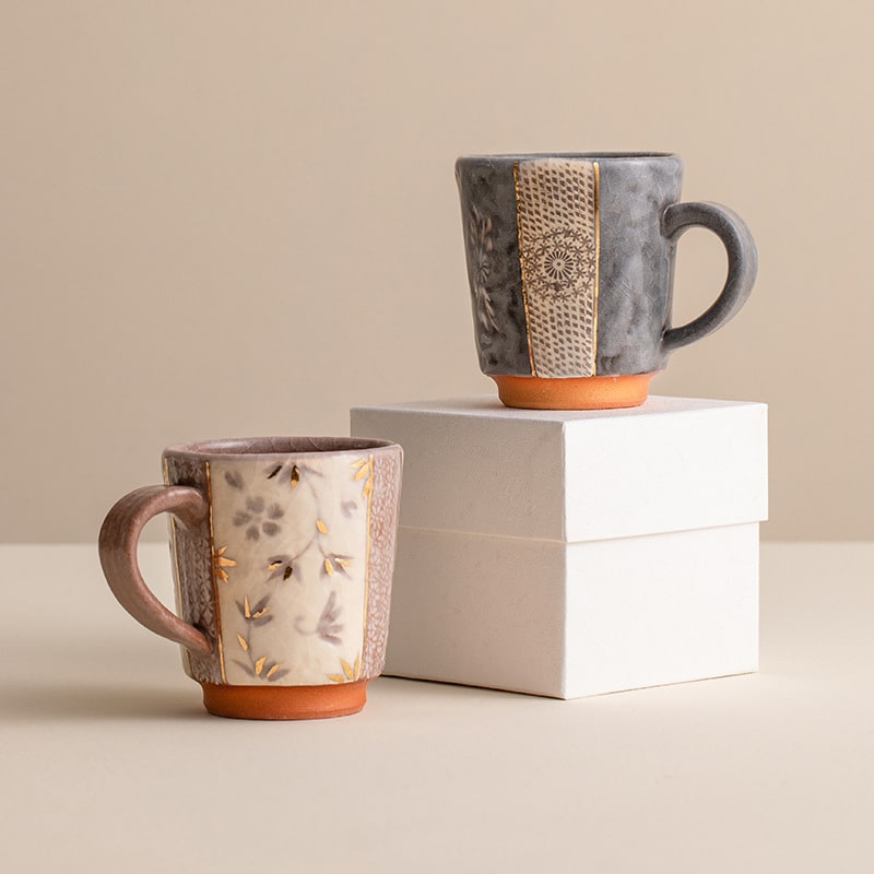 Handcrafted ceramic mug with gold floral details on a wooden table.