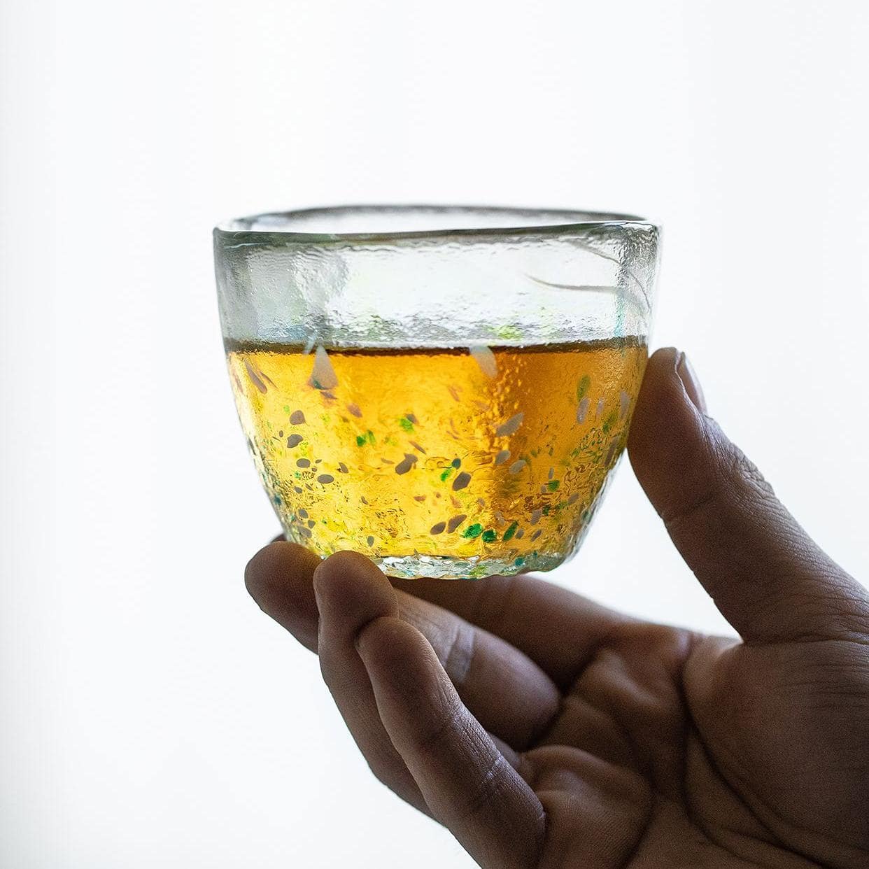 Hand holding a vibrant artisan glass cup against a bright background.