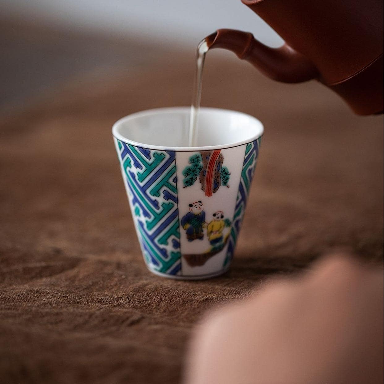 Hand holding a Japanese porcelain cup with intricate details