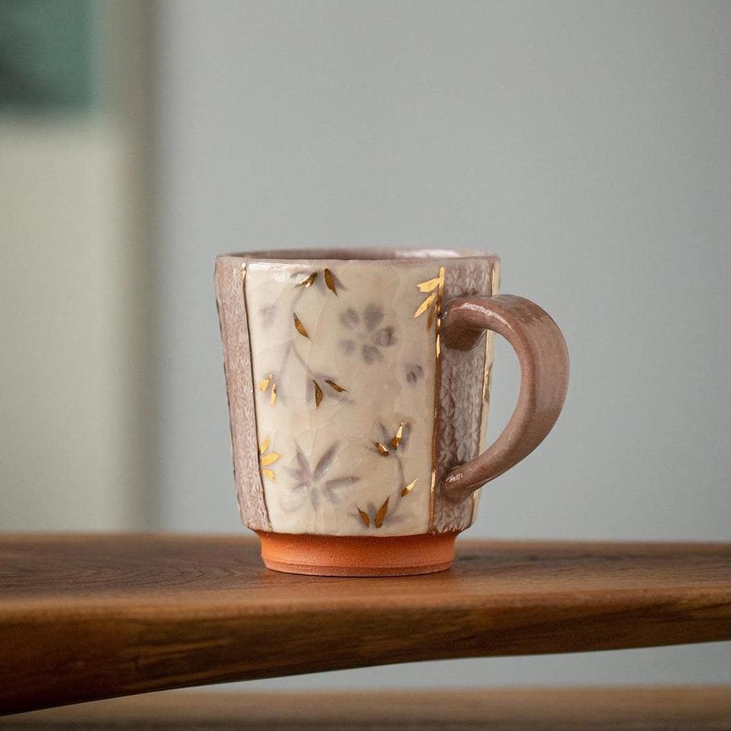 Handcrafted ceramic mug with gold floral details on a wooden table.