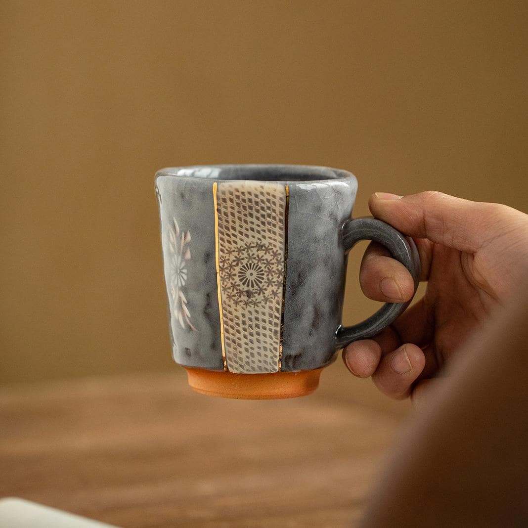 Close-up of textured ceramic mug with gold accents and floral design.