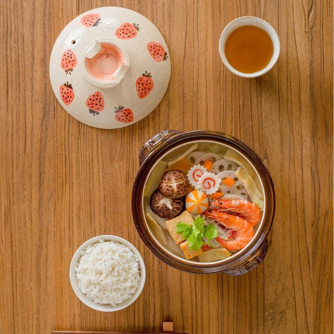 Artisan ceramic donabe pot with whimsical strawberry details.
