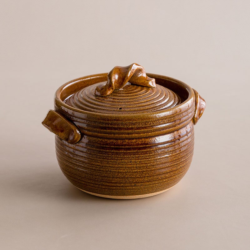 Hand lifting the lid of a black Japanese Shinraku-yaki cooking pot