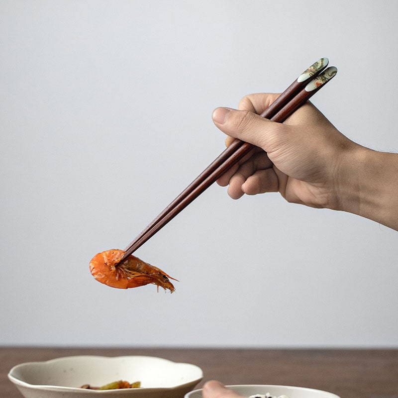 Close-up of hand holding chopsticks with intricate dragon design