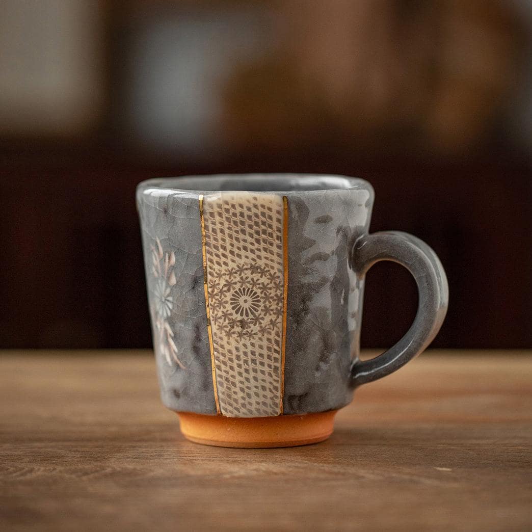 Handcrafted ceramic mug with gold floral details on a wooden table.