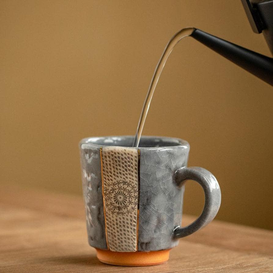 Grey ceramic mug with intricate patterns and a sturdy handle.