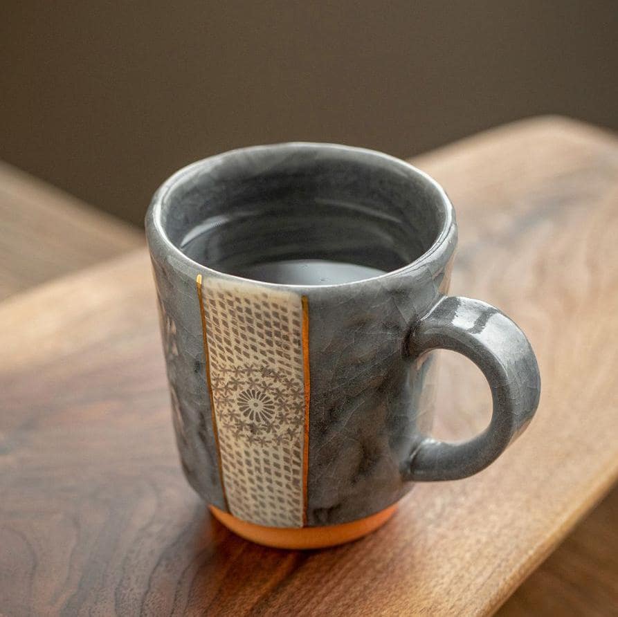 Close-up of textured ceramic mug with gold accents and floral design.