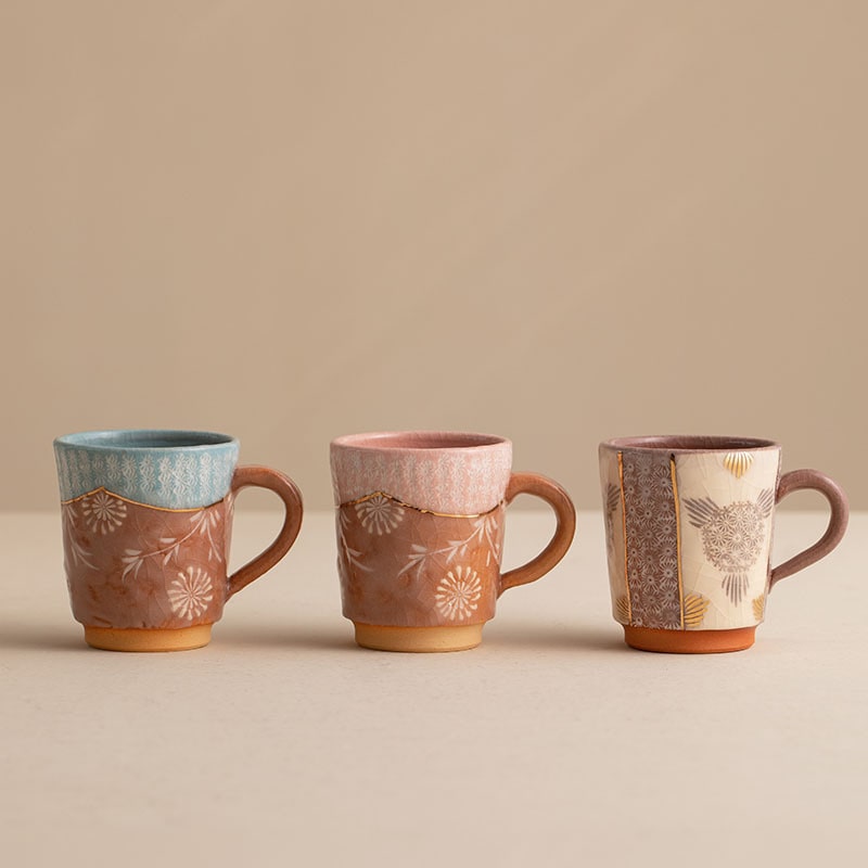 Handcrafted ceramic mugs with floral patterns and gold accents on display