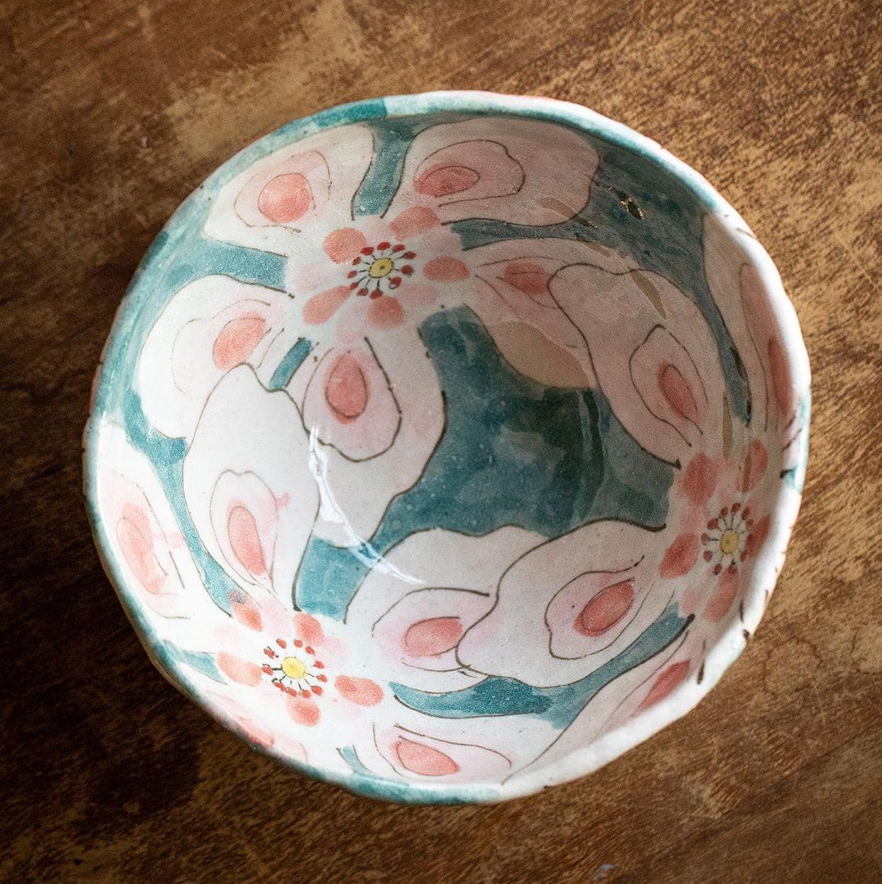 Close-up view of the intricate hand-painted floral pattern on a yellow Japanese ceramic bowl