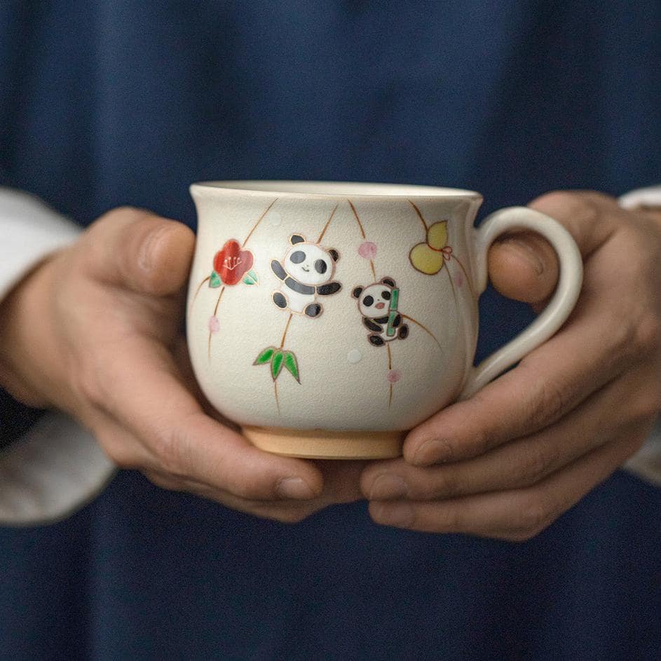 Hand holding a hand-painted ceramic cup with cheerful designs.