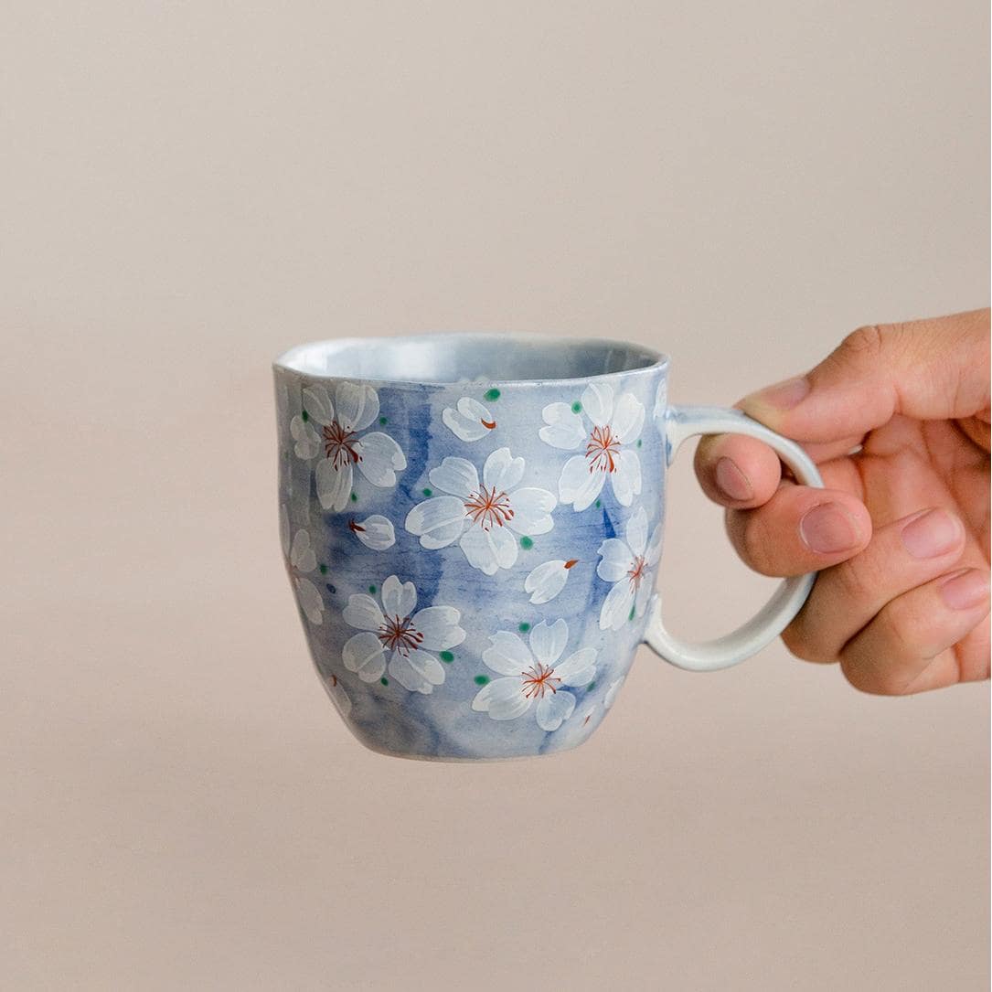 Blue hand-painted cherry blossom coffee cup on a wooden table.