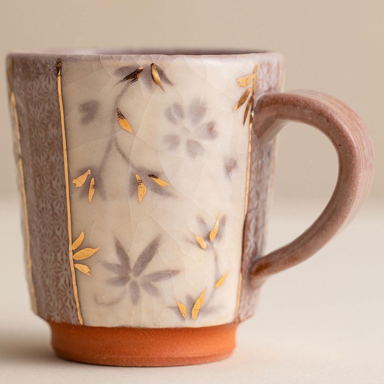 Handcrafted ceramic mug with gold floral details on a wooden table.