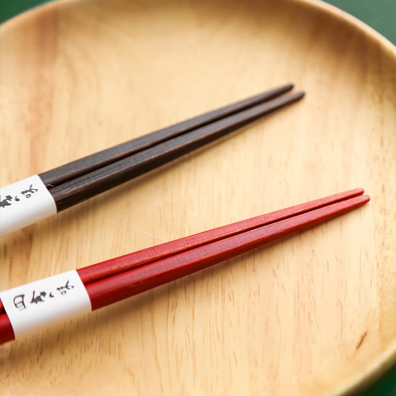 Close-up of red and dark brown bamboo-inspired chopsticks on a wooden plate.