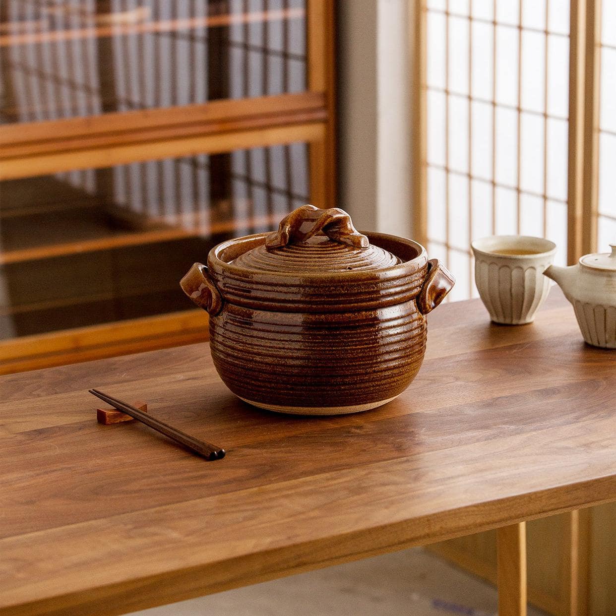 Hand lifting the lid of a black Japanese Shinraku-yaki cooking pot