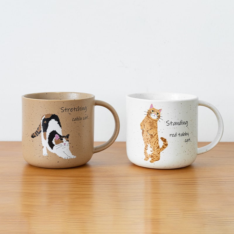 Two adorable ceramic mugs with playful cat illustrations.