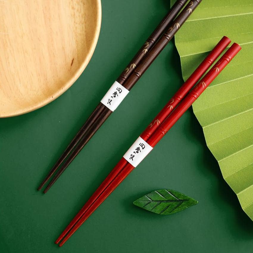 Elegant chopstick set displayed with a natural wood plate and bamboo leaf.