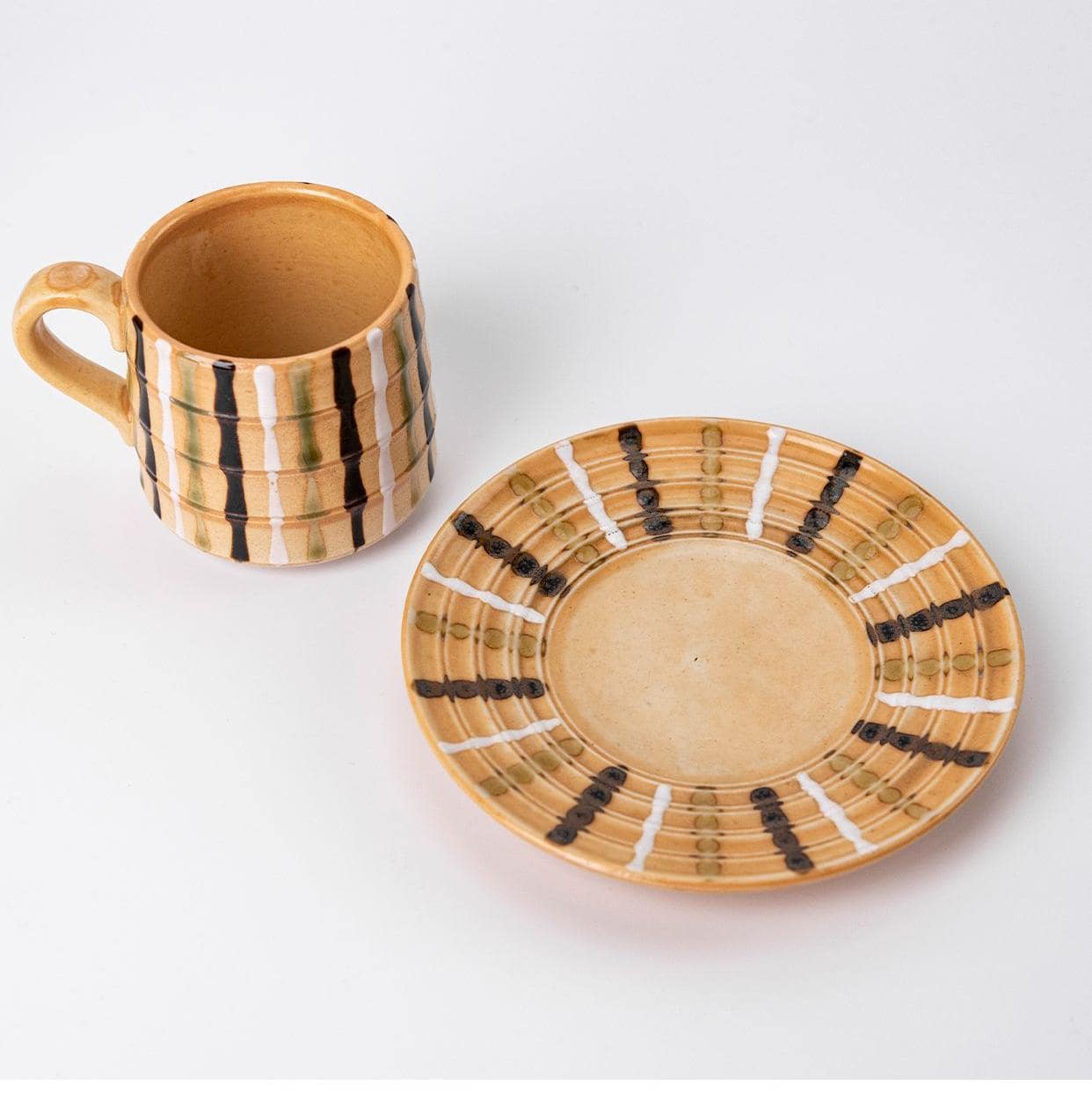 Yellow ceramic mug on a saucer with intricate artistic details.