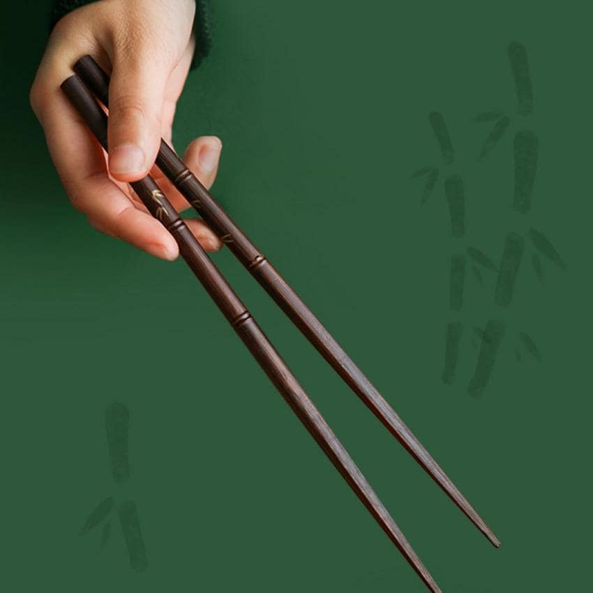 Close-up of red and dark brown bamboo-inspired chopsticks on a wooden plate.