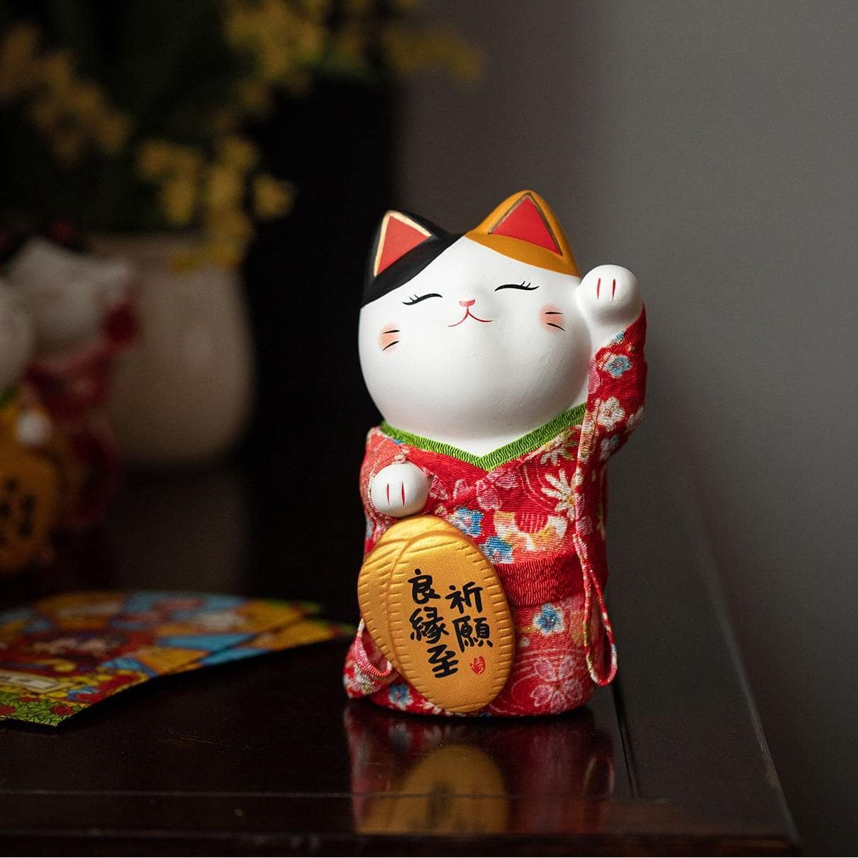 Japanese ceramic lucky cat figurine in a red kimono on a wooden table.