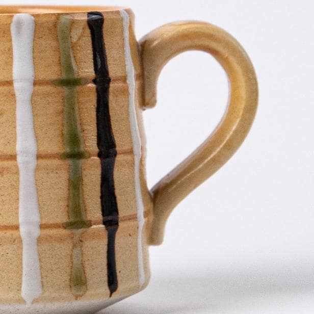 Vibrant yellow striped ceramic mug and saucer on a wooden table.