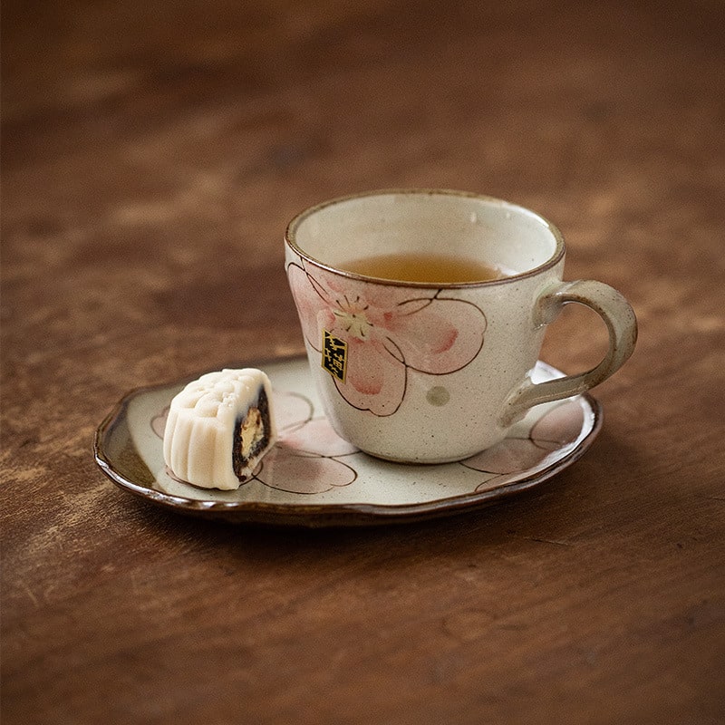 Hand-painted ceramic tea cup with sakura blossom design and saucer.