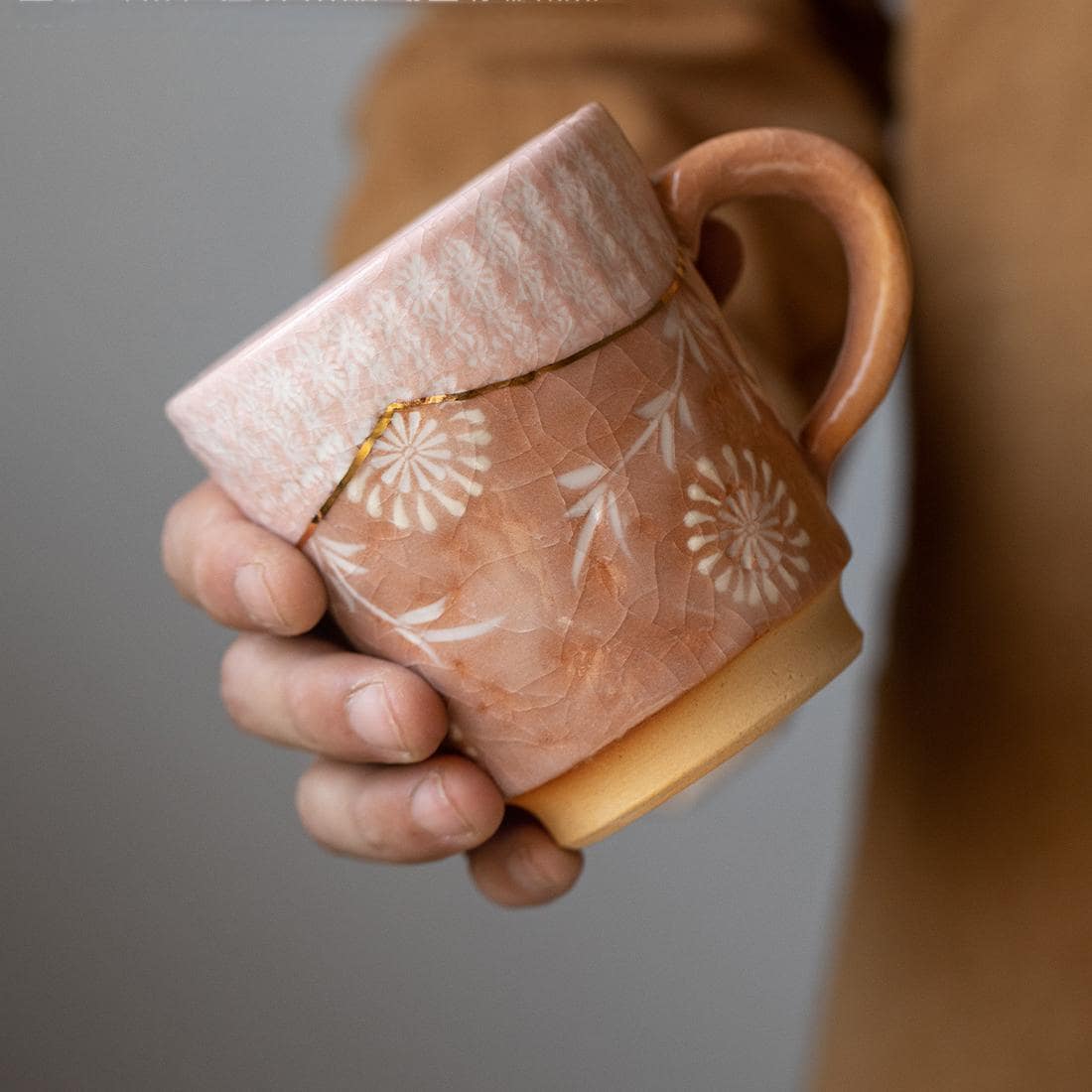 Handcrafted ceramic mugs with floral patterns and gold accents on display