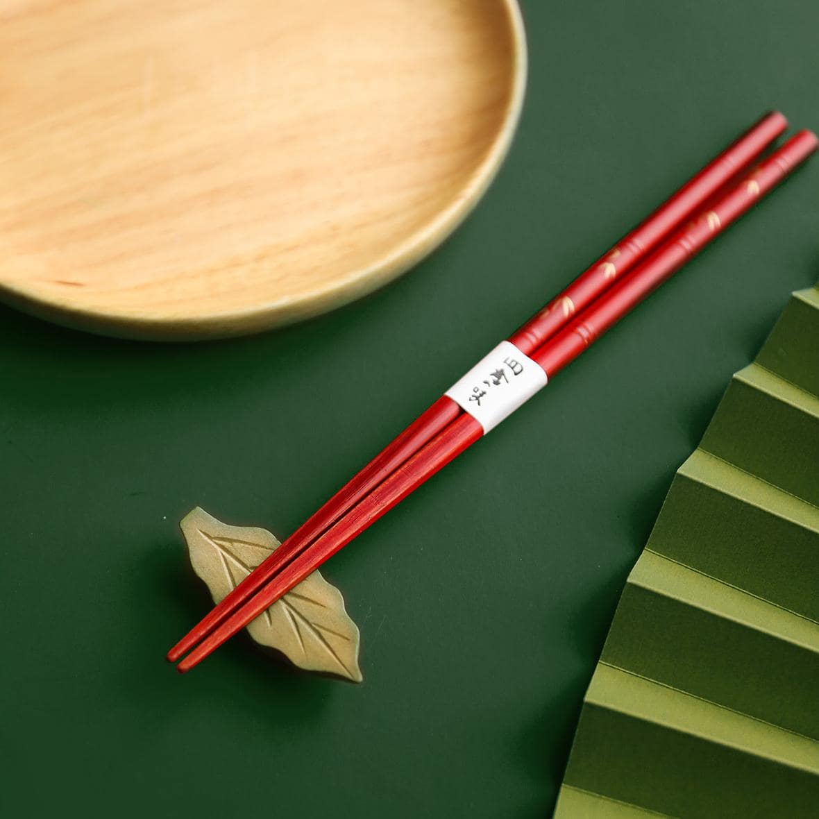 Elegant chopstick set displayed with a natural wood plate and bamboo leaf.