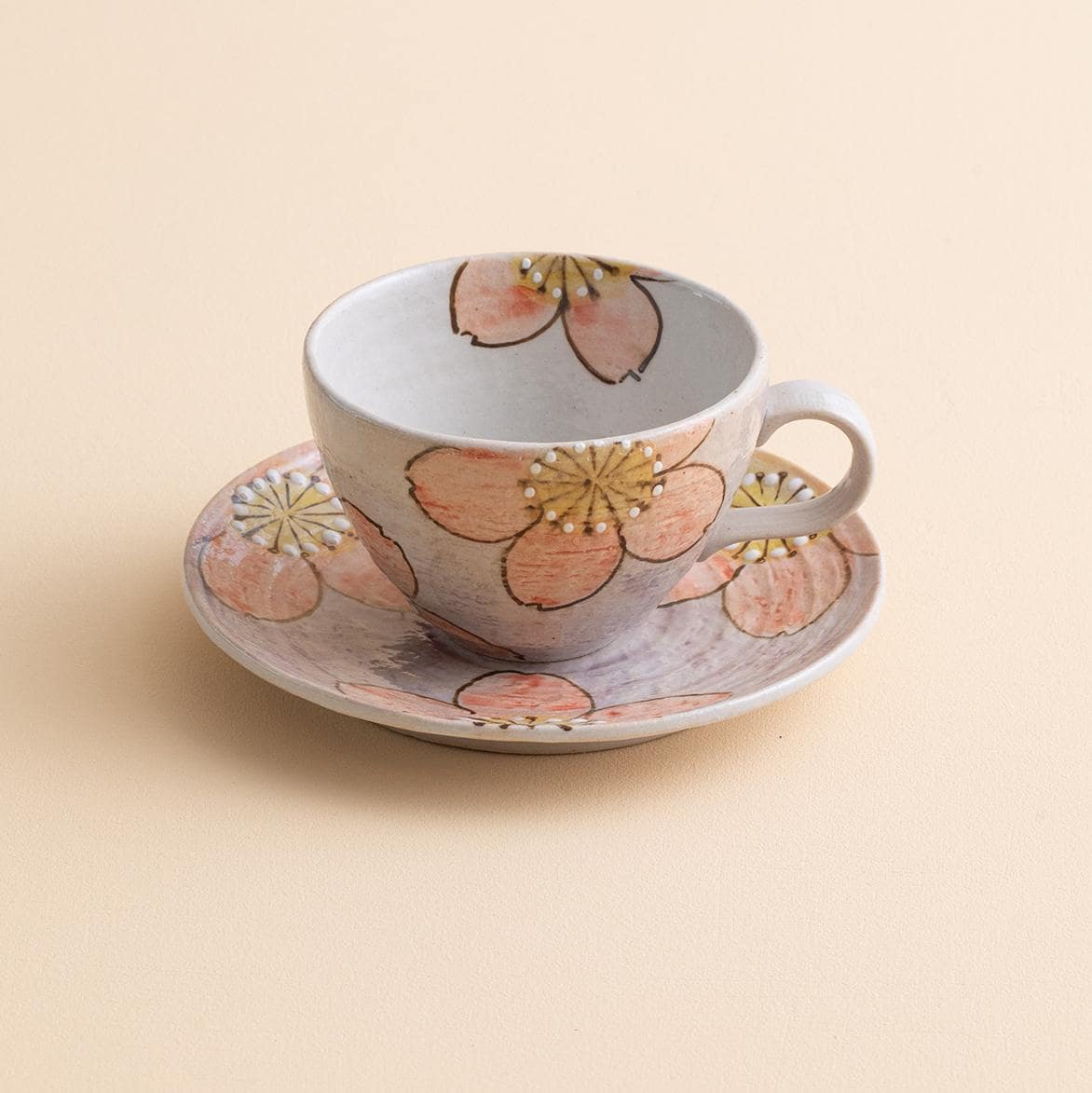 Hand-painted ceramic tea cup with sakura blossom design and saucer.