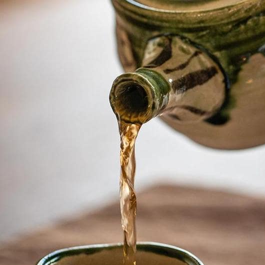 Artisan-crafted Oribe teapot pouring tea into a matching cup.