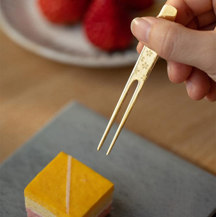 Hand holding a gold-plated dessert fork with floral engravings