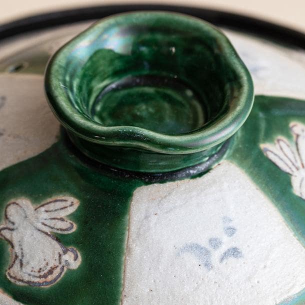 Close-up of hand-painted green and white rabbit design on Oribe pot