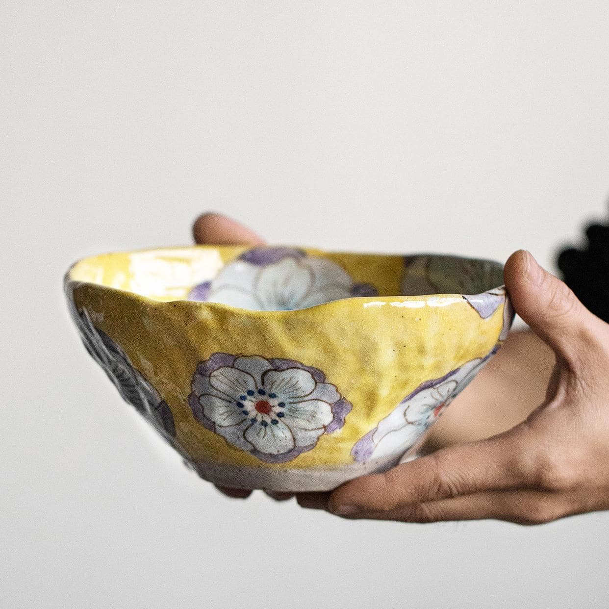 Close-up view of the intricate hand-painted floral pattern on a yellow Japanese ceramic bowl