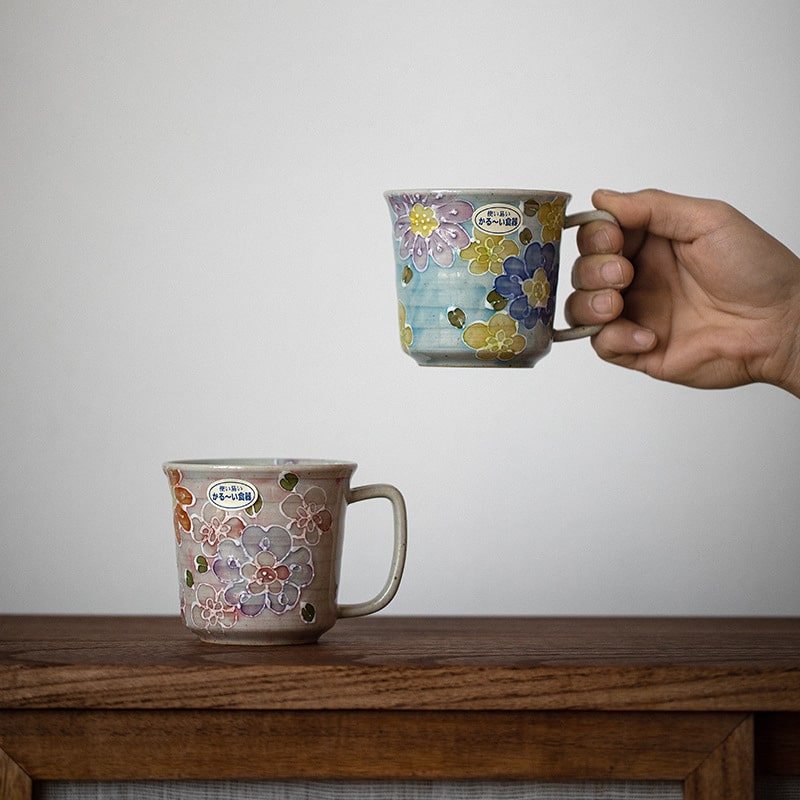 Hand holding a floral ceramic mug with vibrant colors