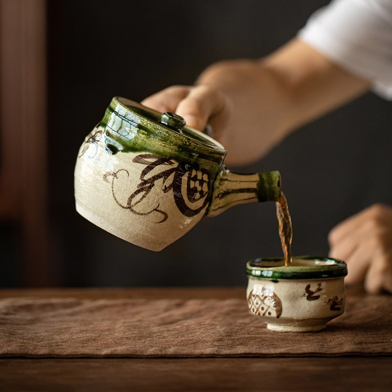 Artisan-crafted Oribe teapot pouring tea into a matching cup.