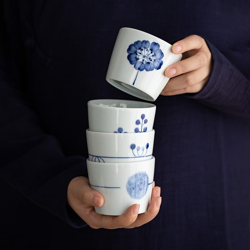 Stack of blue and white porcelain tea cups with nature-inspired designs.