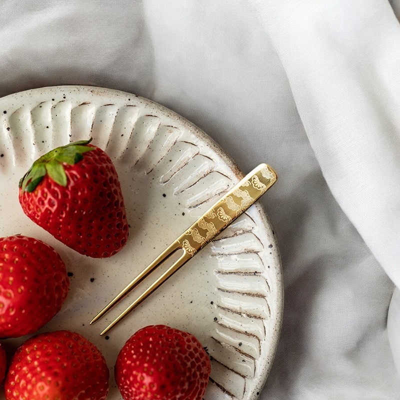 Hand holding a gold-plated dessert fork with floral engravings